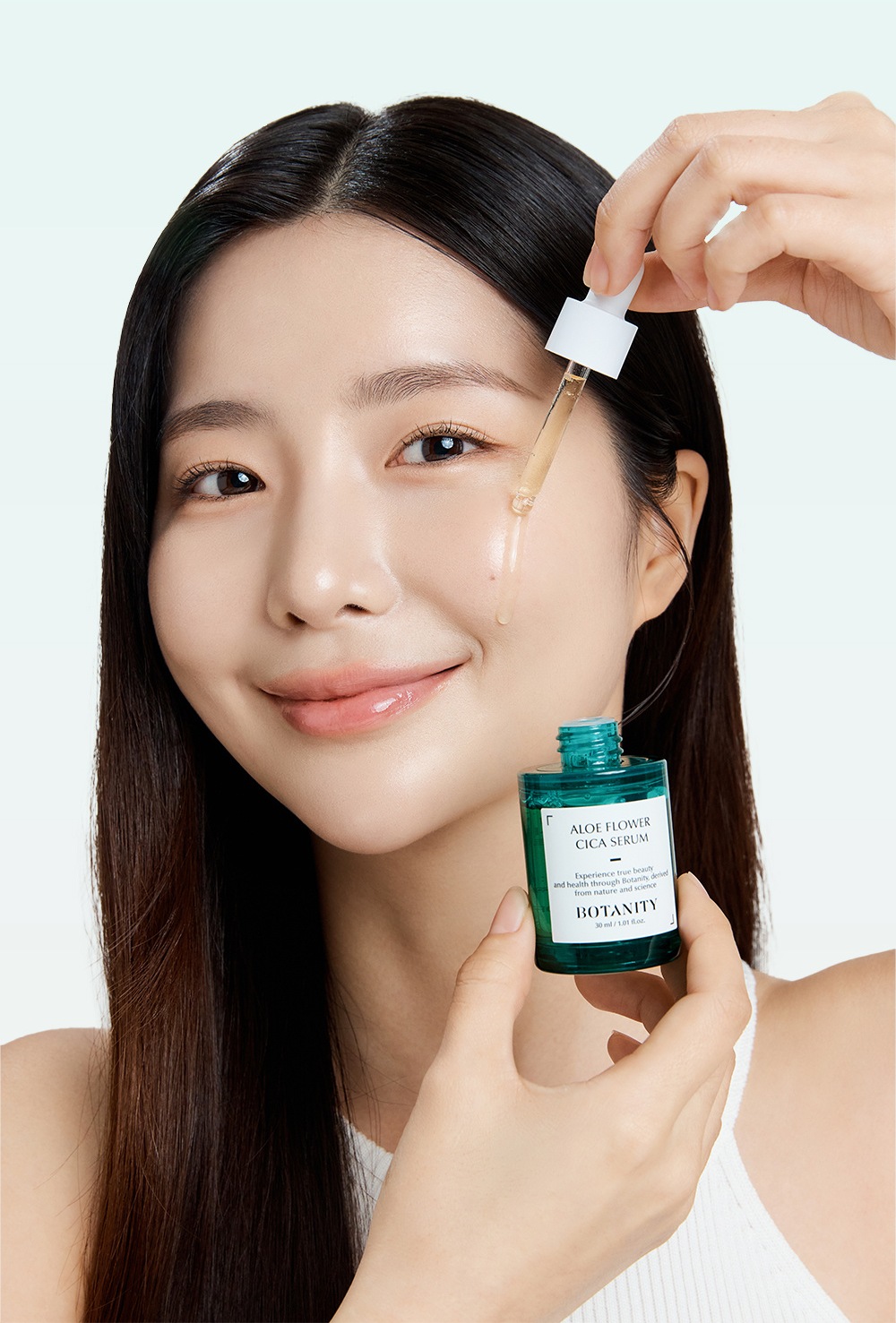모델이 스포이트로 눈가 옆 피부에 세럼을 떨어뜨리며 다른 손에 알로에 플라워 시카 세럼 병을 든 사진