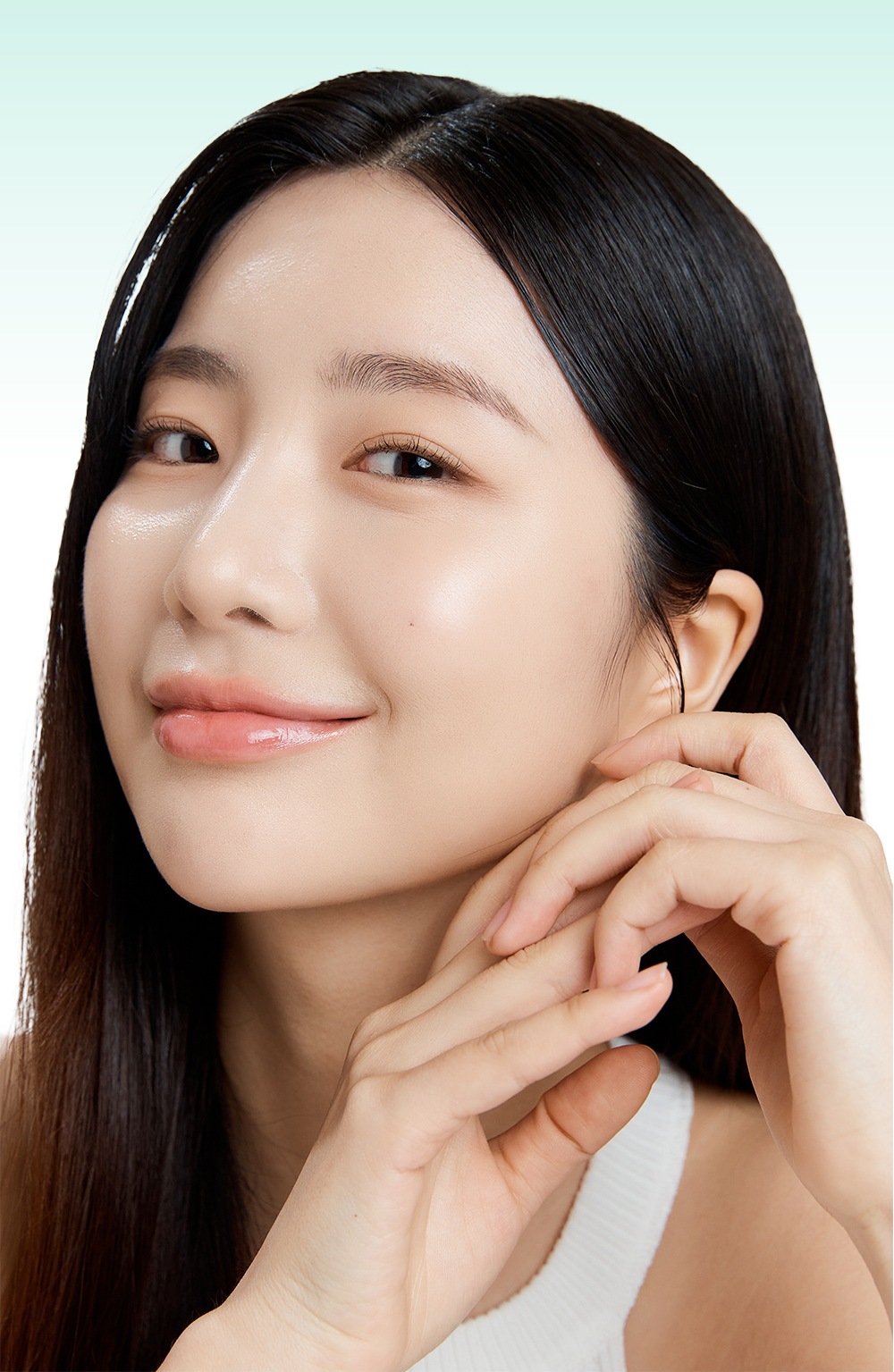긴 검은 머리의 모델이 턱선에 두 손을 모아 대고 미소 짓는 얼굴 사진, 흰 민소매